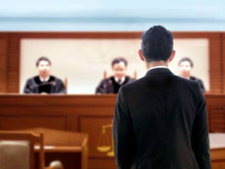 A person in a suit stands in front of a judge