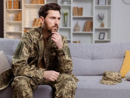 A man in camouflage attire is seated on a couch
