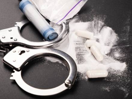 A close-up of handcuffs and pills arranged on a black background, representing issues of substance abuse and restraint.