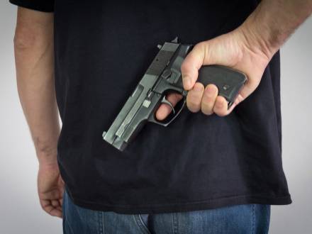 A man stands with a gun tucked in his back pocket